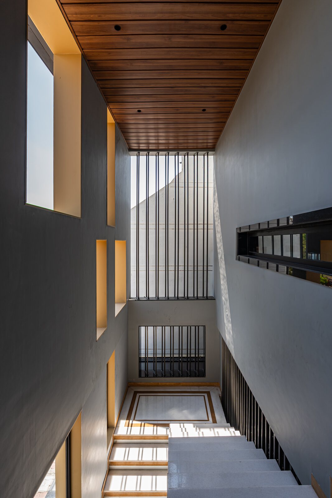 The double-height stair, vertical fins climbing to a timber ceiling.