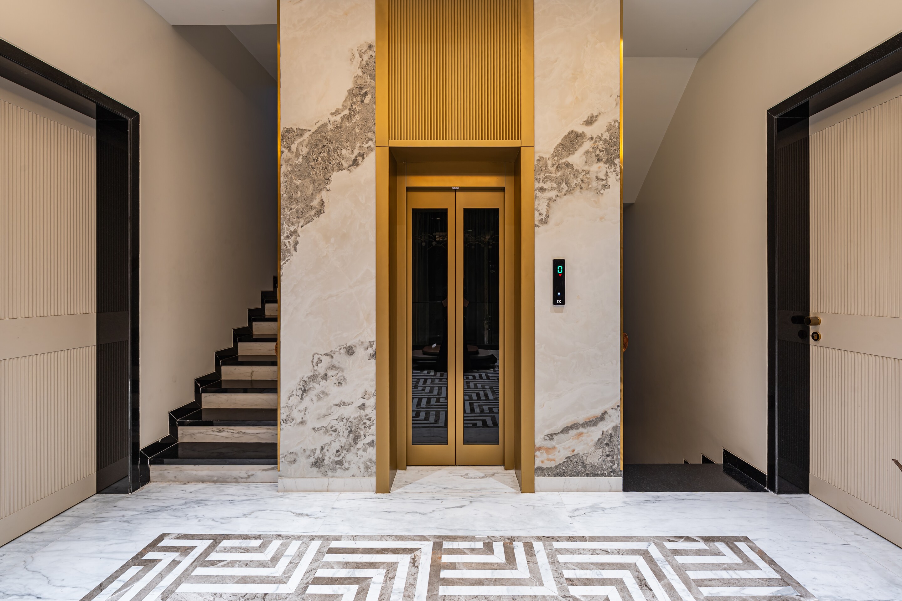 The lift in marble, a greek-key floor at its foot.