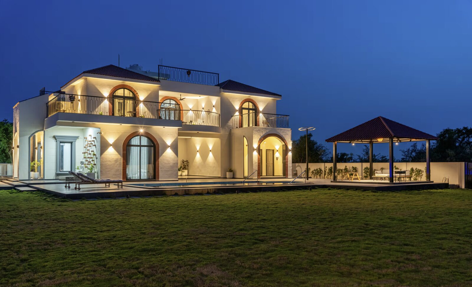 The villa at dusk, arched windows lit above the lawn.