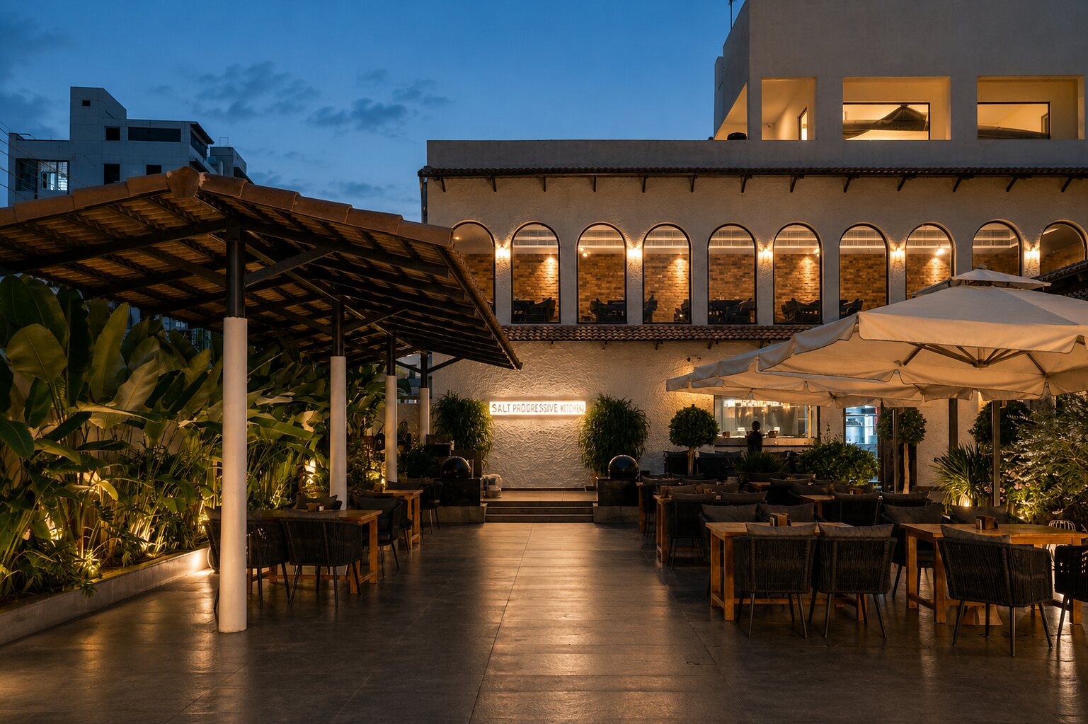 The terrace at dusk, lanterns lit beneath the umbrellas.
