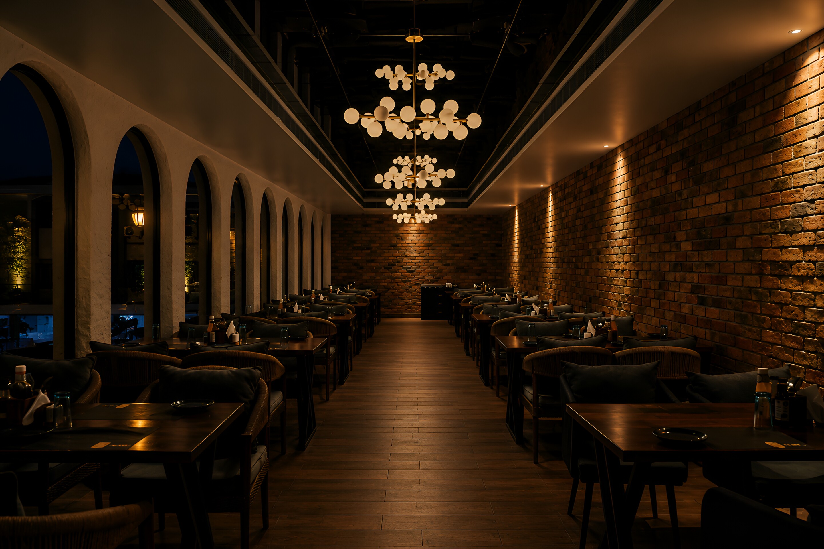 The long dining hall at dusk, brick and a low chandelier.