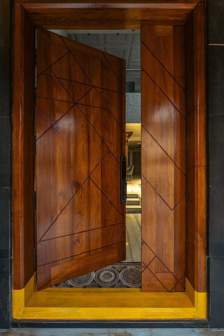 The teak front door, brass inlay in a grooved field.