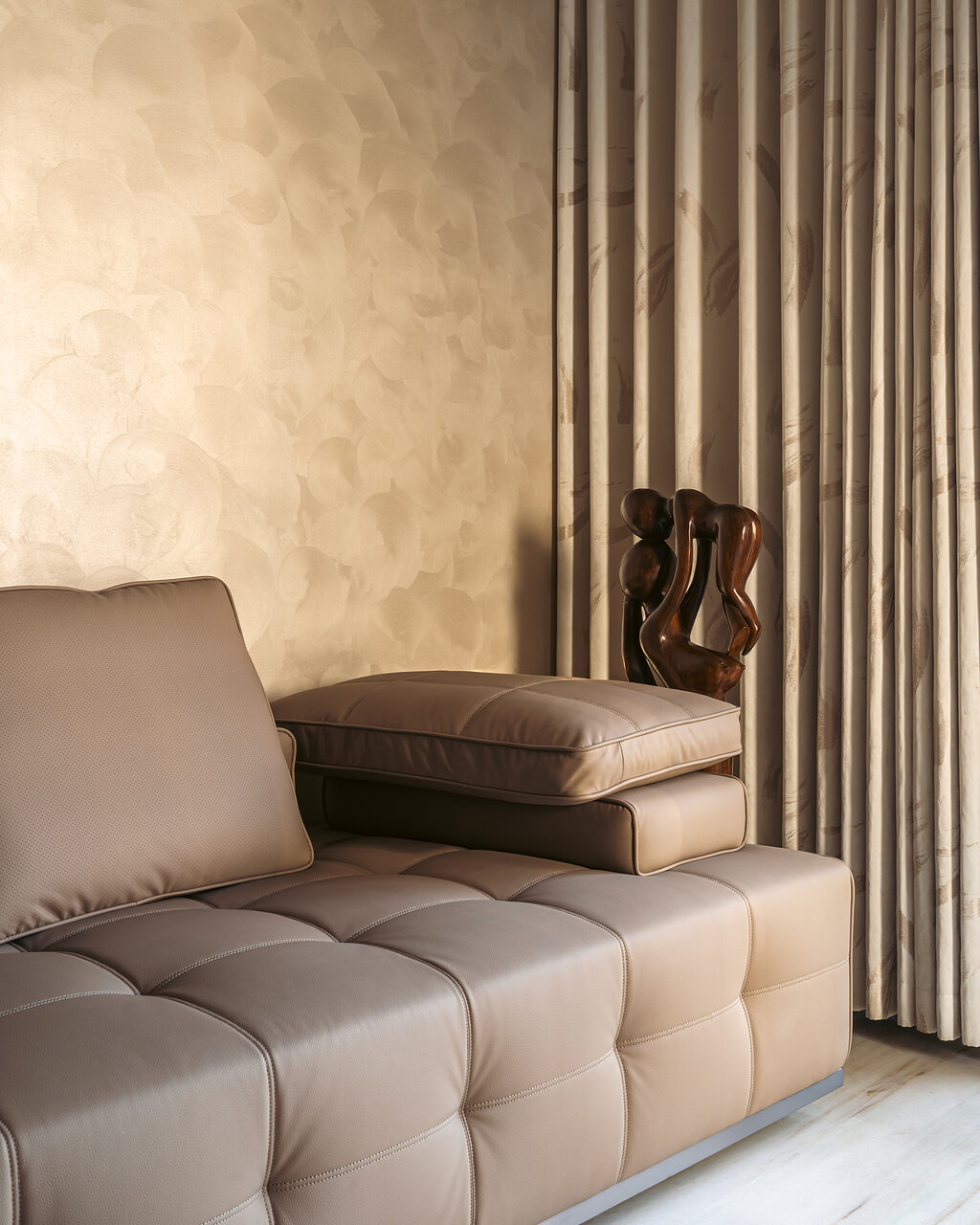 A chaise and round table beside a textured curtain.